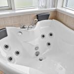 Eckbadewanne mit Duschkopf und mehreren Massagehöhlen.