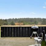 Terrasse mit Grill, Tisch und Stühlen. Hintergrund: Wald und Himmel.