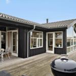Haus mit Holzterrasse, Grill und Sitzgelegenheiten. Fenster und Türen zeigen Innenräume.