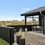 Terrasse mit Tisch, Stühlen und Grill. Schwarze Holzwand, Pflanzen und Dachüberstand.