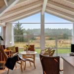Großes Wohnzimmer mit Blick auf Wald. Holzdecke, große Fenster, Möbel.