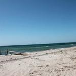 Strand mit Holzsteg und klarem Himmel. Sandstrand mit Wellen.