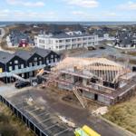 Neubau mit Scaffolding in Strandnähe, umgeben von Häusern und Dünen.