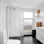 Badezimmer mit Dusche, Waschbecken und Toilette. Weiße Fliesen und dunkle Bodenfliesen.