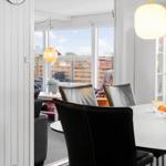 Essbereich mit schwarzen Stühlen und weißem Tisch. Durchgang zum Wohnbereich mit großem Fenster.