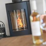 A wood-burning stove with fire. On the table, a glass and a bottle.