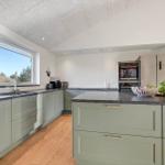 Modern kitchen with green cabinets, stone countertops, and view of nature.