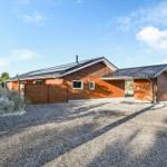 Wooden house with roof and garage on gravel ground. Surrounded by trees and sky.