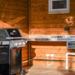 Outdoor kitchen with grill and stainless steel sink against wooden wall