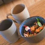Two mugs and a bowl with sweets on wooden table.