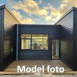 Modern wooden house with large window and deck under cloudy sky.