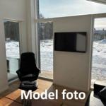 Room with black seating, wall-mounted TV, and large windows for views.