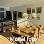 Dining area with wooden table, chairs, and kitchen island in background.