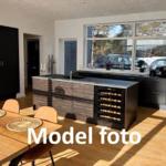 Kitchen with dining area, wooden floor, and large window. Stainless steel countertop and wine rack.