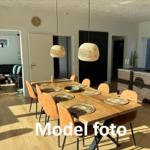 Dining area with wooden table, chairs, and pendant lamps. Kitchen and living room in background.