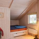 Schlafzimmer mit Holzwand, Bett und Fenster. Ein kleiner Holztisch steht daneben.