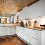 Küche mit weißen Schränken, Holzdecke und Terrakottboden. Auf der Arbeitsfläche steht ein Laib Brot.