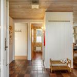 Hausflur mit Holzdecke, gefliestem Boden und Schuhbank. Tür führt ins Bad.