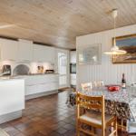 Küche und Essbereich mit Holzdecke, weißen Schränken und Steinbelag am Tisch.
