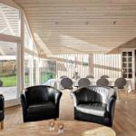A room with wooden ceiling, black chairs, and large windows overlooking the garden.