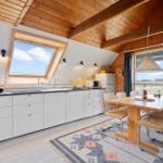 Küche mit Essbereich, Holzdecke und großem Fenster. Tisch mit Stühlen und Teppich.