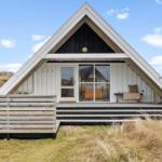 A-frame-Haus mit Holzveranda und Glasfront. Umgeben von Gras und blauem Himmel.