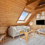 Wohnzimmer mit Holzwand, Sofa, Sessel und TV. Dachfenster und helle Bodenplanken.