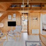 Wohnraum mit Holzwänden, Sofa, Sessel und Fernseher. Durchgang zu Schlafzimmer und Küche.