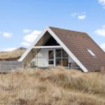 A-frame-Haus mit braunem Dach und Holzverkleidung, umgeben von trockenem Gras unter blauem Himmel.