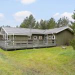 Green holiday home with wooden terrace and view of forest.