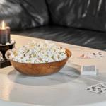 Table with popcorn bowl, playing cards, and lit candle in front of a sofa.