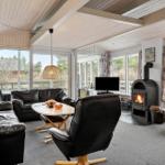 Living room with fireplace, sofa and armchair. Large windows with view of outdoor area.