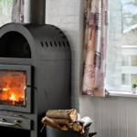 Wood stove with burning fire, firewood, and windows with curtains.