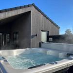 Steamy hot tub in front of a wooden house with large window area.