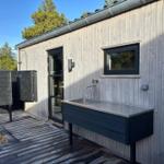 Outdoor area with sink, shower, and wooden terrace beside a house.