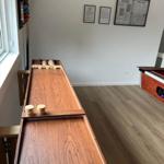 Long wooden table with game pieces and wall rack in room with wooden floor.
