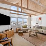 Wohnzimmer mit Holzboden, TV, Sofa und Blick auf verschneite Landschaft.