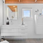 Badezimmer mit weißem Waschbecken, Spiegel und Fenstern.
