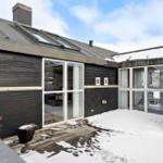 Schwarze Holzwand mit Glasfront und Schneedecke im Hofbereich.