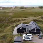Schwarzes Haus mit Terrasse und Parkplatz in Dünenlandschaft mit Blick aufs Meer.
