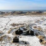 Schwarzes Haus auf schneebedeckten Dünen mit Blick auf das Meer.