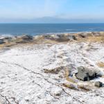 Schneebedeckte Dünenlandschaft mit Strandhaus und Blick auf das Meer.