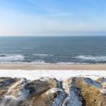 Meer und Strand mit schneebedeckten Dünen im Vordergrund.