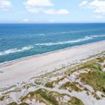Weiterer Blick auf den Strand mit Dünen und Meer.