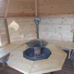 Wood sauna with hanging grill and benches around fire pit