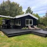 Black house with terrace, lounge chairs, and garden.