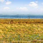 Weiteres Uferland mit Blick auf das Wasser und fernen Horizont.