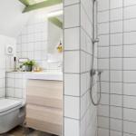 Badezimmer mit Dusche, Waschbecken und Toilette. Weiße Fliesen und Holzfronten.