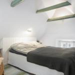 Schlafzimmer mit Bett, Wickerstuhl und grünen Akzenten unter schrägen Deckenbalken.