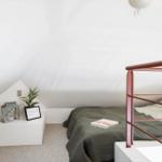 Schlafzimmer mit Dachschräge, Bett mit Metallgestell und Nachttisch mit Pflanze und Laterne.